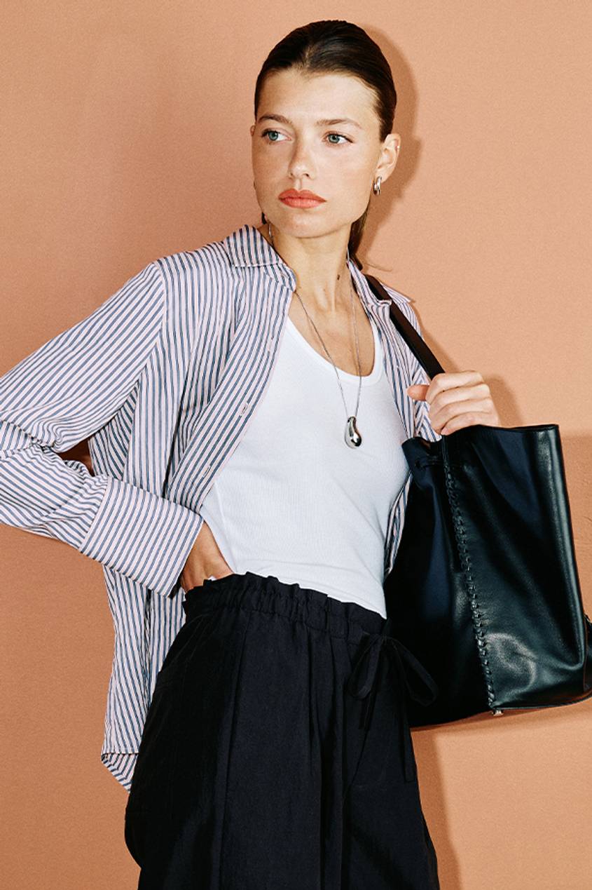 Woman wearing a striped long sleeve shirt with a white tank, black pants, and a black leather shoulder bag.