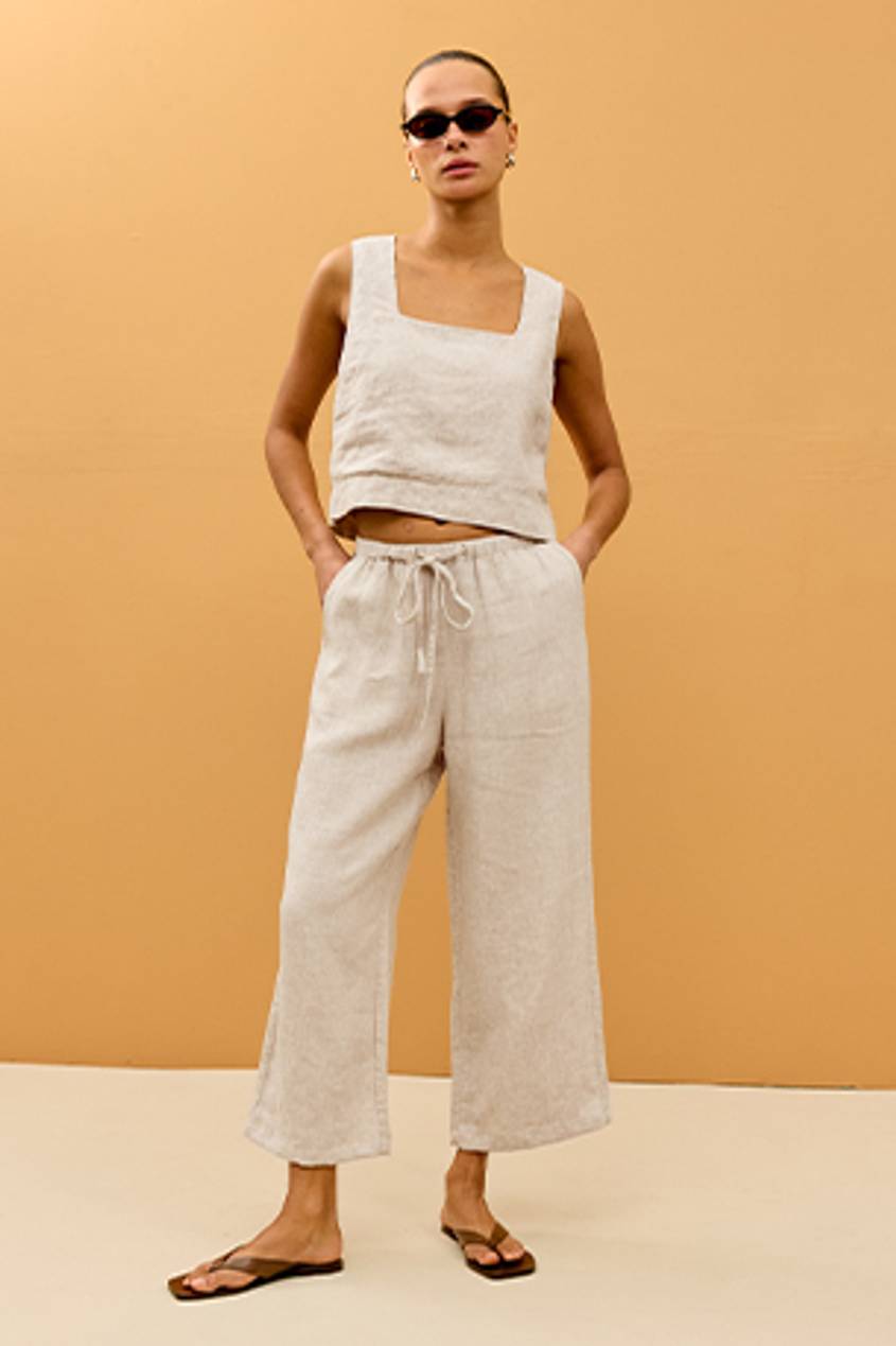 Woman posing in a beige linen set against an orange background.