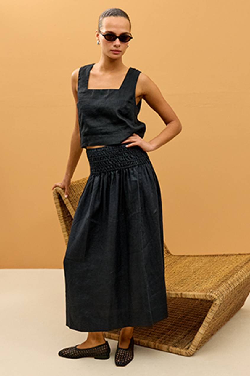 Woman wearing an all black maxi skirt linen set paired with black flats.