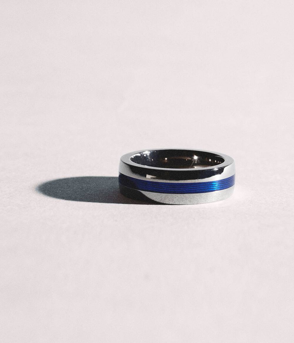 A silver Geo blue enamel ring laying flat creating a dark shadow.
