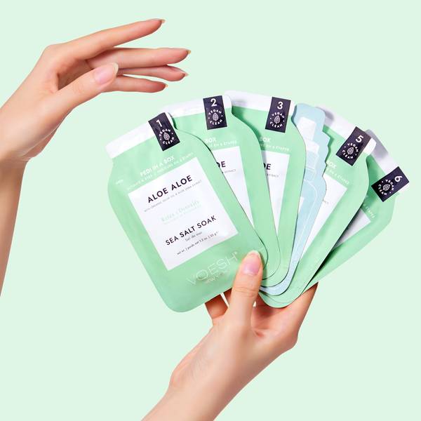 Hands Holding Pedi In A Box Ultimate 6 Step Aloe Aloe Packets on Green Background