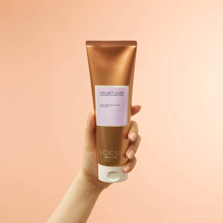 Woman's hand holding lavender relieve 8 oz hand & body creme on a pink background