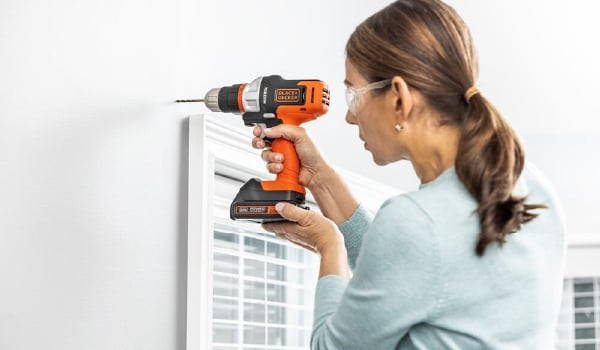 Woman drills hole into drywall to prepare to hang curtains using the BLACK+DECKER MATRIX drill attachment.