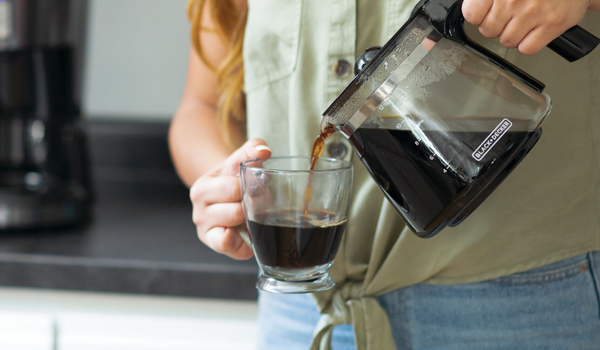 woman pouring coffee from a pot into a clear, glass mug