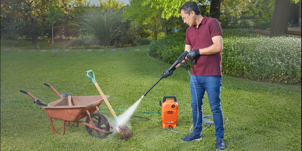 Man using BLACK+DECKER 1,700 MAX psi* pressure washer with 40˚nozzle to clean dirt off of a shovel and wheelbarrow