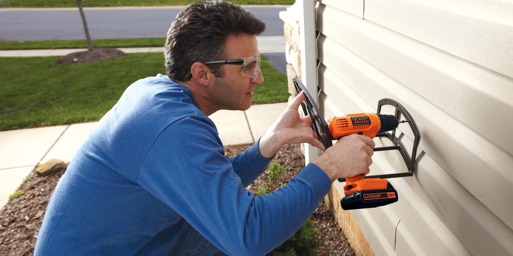 Lithium drill and driver with 30 accessories being used by a person to drill into the exterior of a house.