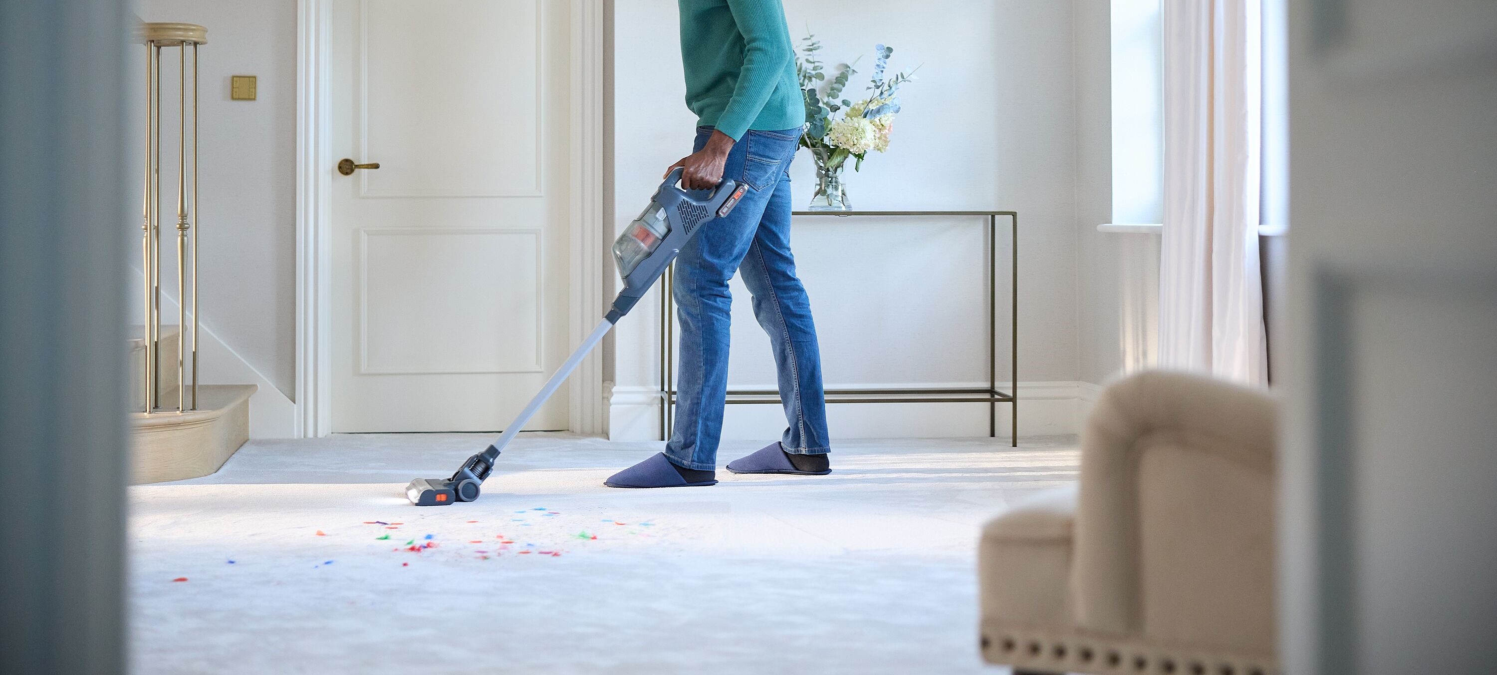 A man vacuums a carpet floor with the BLACK+DECKER® POWERSERIES+™ 18V 2-in-1 Stick Vacuum.