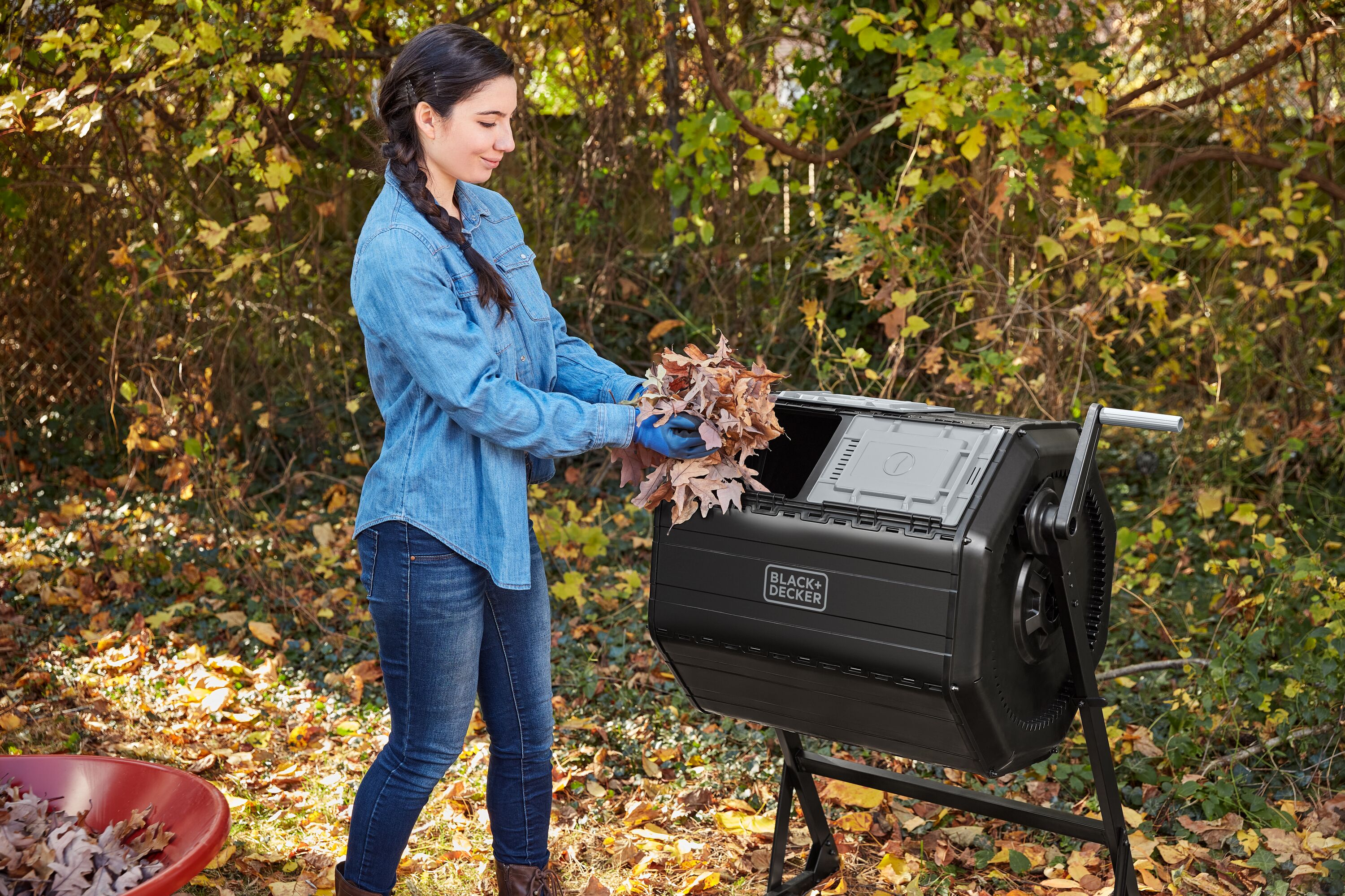 Woman putting leaves in the left chamber of the BLACK+DECKER 40 Gallon Dual Chamber Tumbler Composter