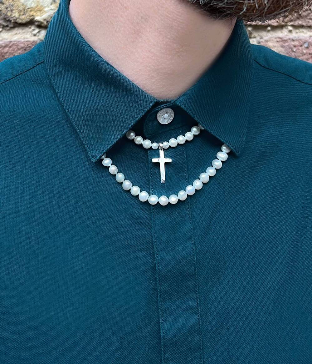 Man in green shirt is wearing a white round pearl with a cross in the middle necktie and a one strand white pearl necklace under his collar.