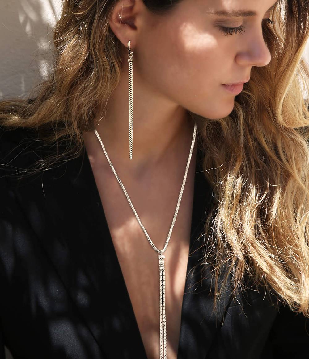 Woman with long hair and a black low cut top is wearing a shimmer necklace in silver with a shimmer hoop earring in silver