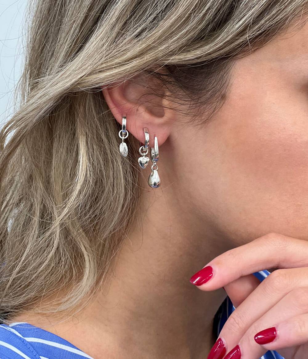 A woman is wearing leaf, heart and water drop silver earrings.