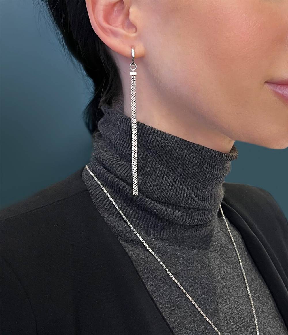 Woman in grey turtleneck top wearing a silver shimmer charm earring attached on a silver hoop.