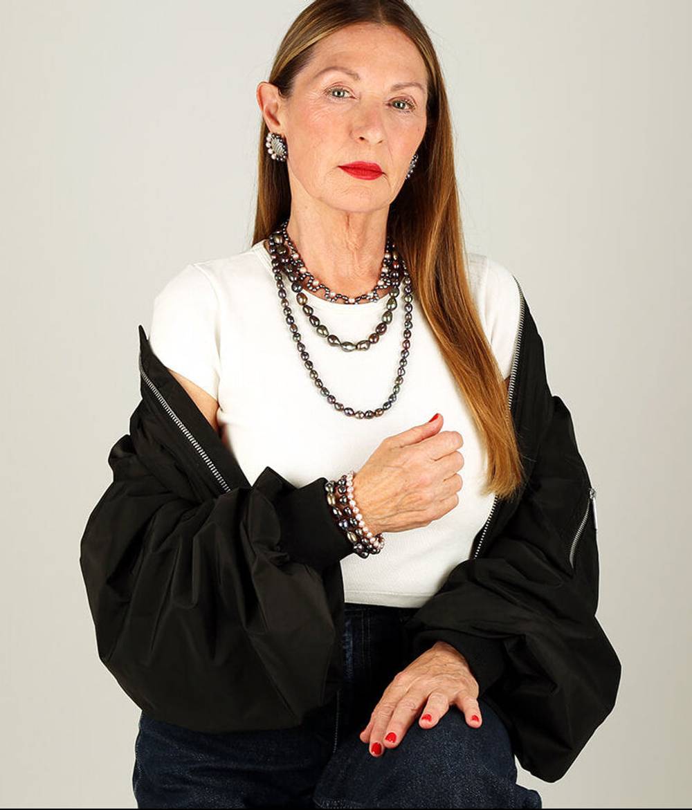 Woman wearing a three strand peacock pearl necklace and matching bracelet and earrings.