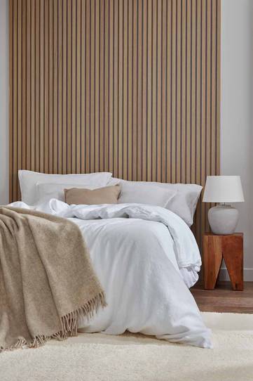 Roomset image showing oiled Natural Oak slatwall panel on a grey felt backing behind a bed with white duvet and pillows.