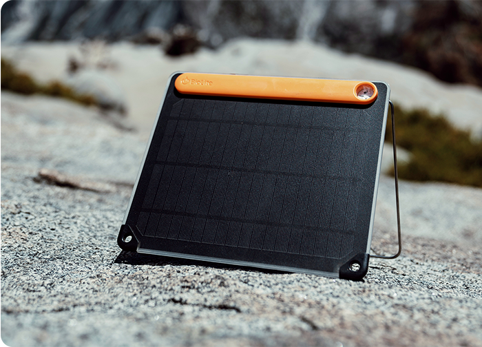 A compact solar panel with a black surface and an orange top, placed on a rocky outdoor surface.