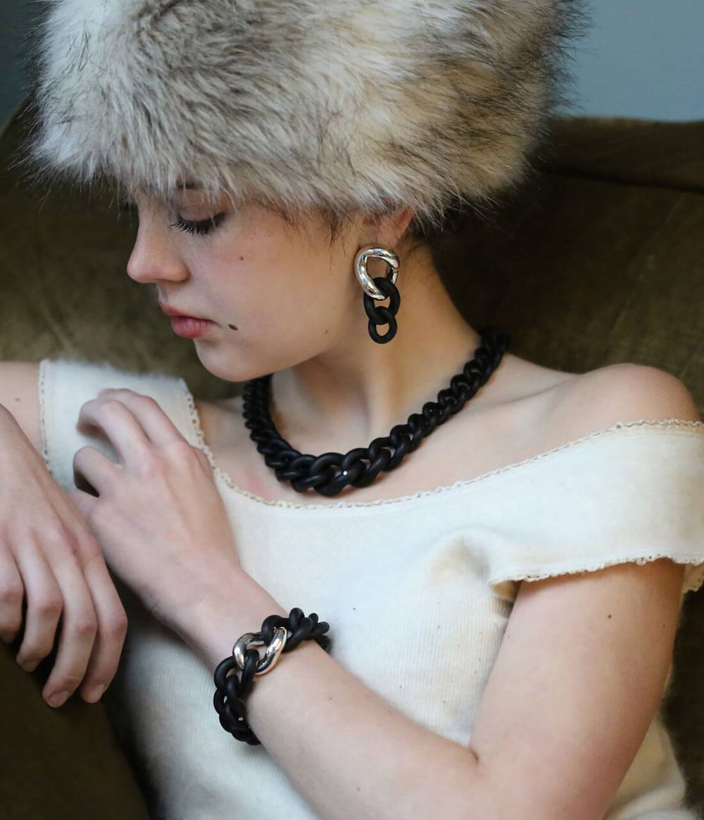 A girl wearing the black caster seed necklace with diamond and the silver and caster seed earrings and bracelet from the Raven jewellery collection.