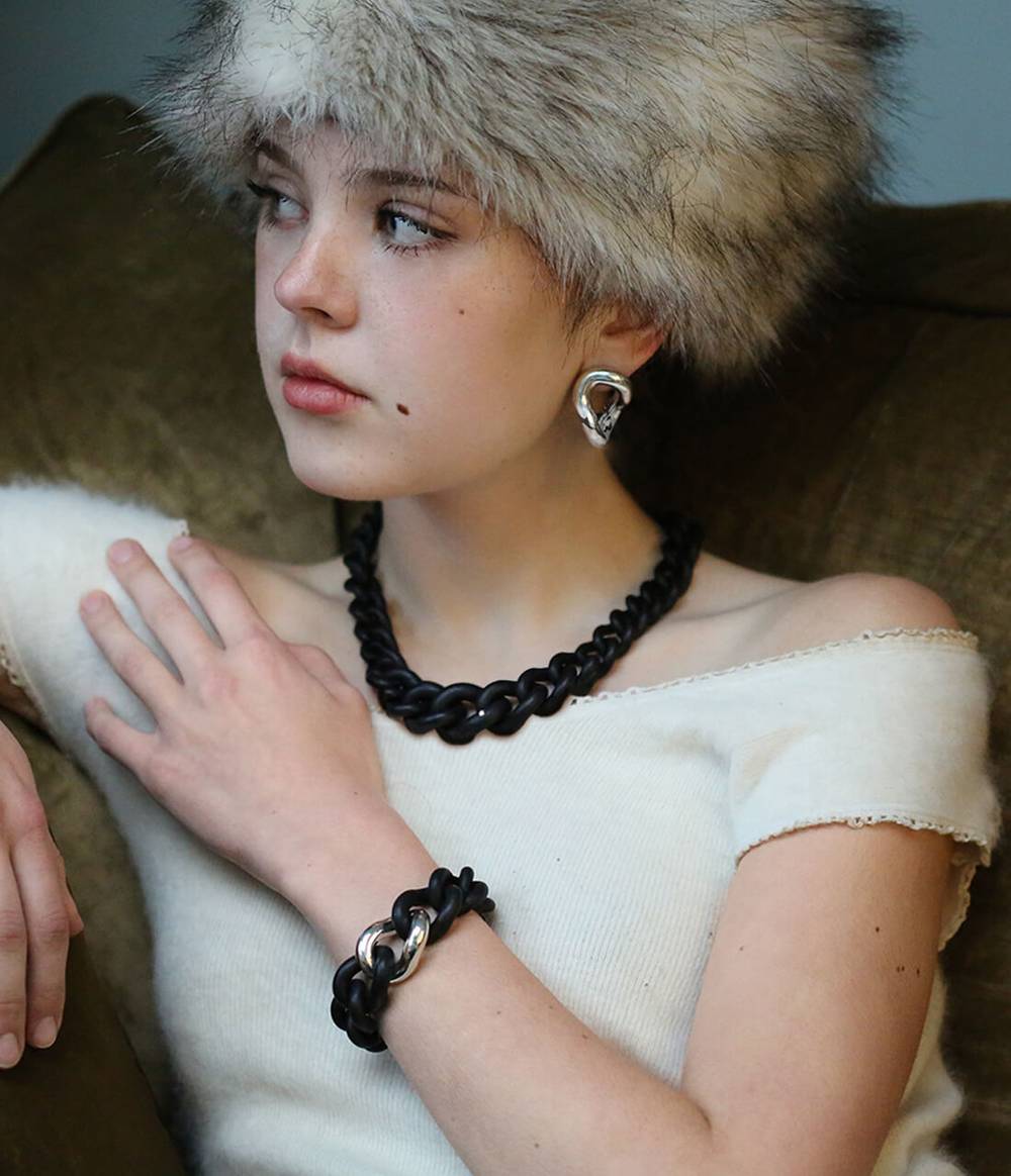 Girl wearing a black necklace with a diamond, a black and silver necklace and a silver earring from the Raven collection.
