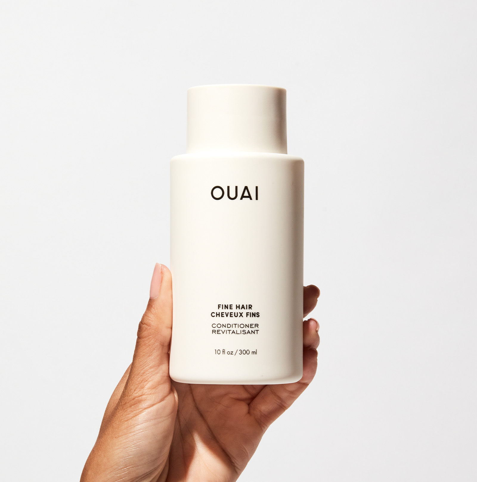 Hand holding a OUAI conditioner bottle against a white background