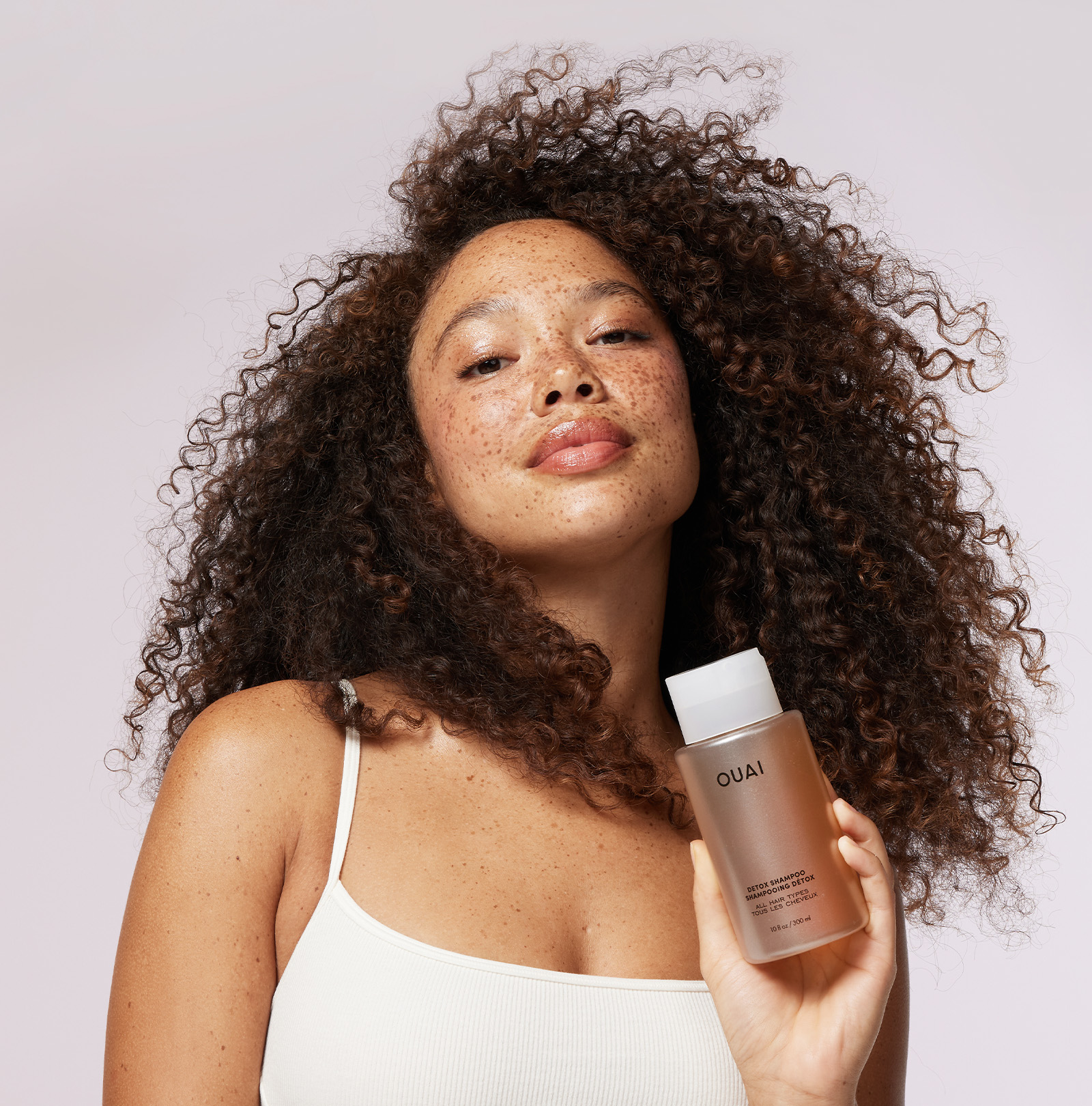 Woman holding a OUAI product against a plain background