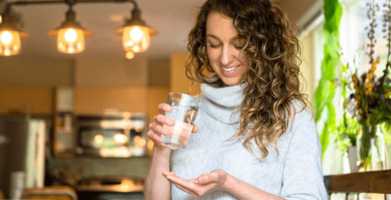 young lady in her kitchen taking U Perform Active Berries with a glass of water