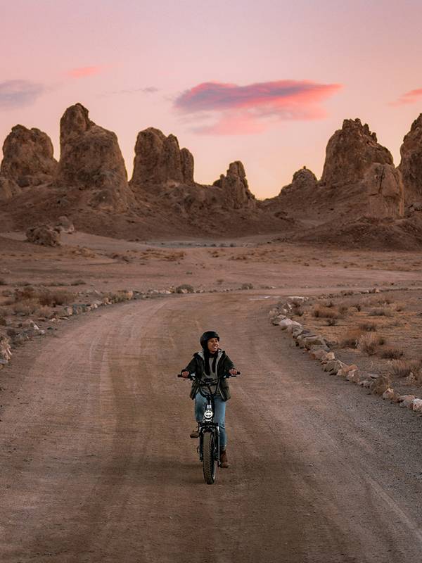 Person riding an electric bike on a dirt trail at sunset with desert in the background