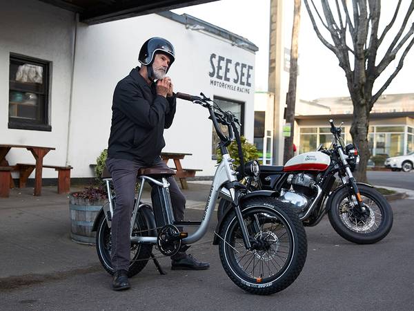 A person standing over a RadRunner Plus ebike adjusts their helmet