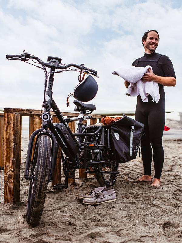 A person wearing a wetsuit stands next to a RadWagon cargo ebike on the beach