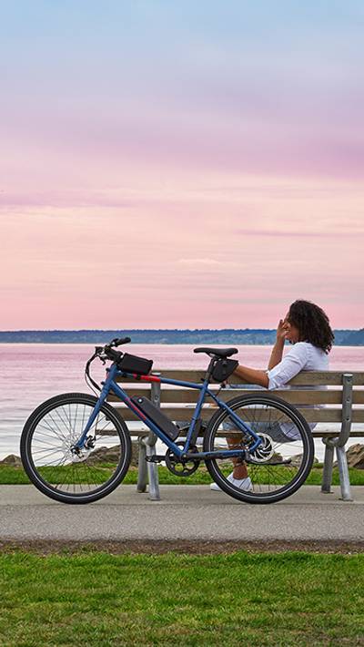 Woman sitting seaside at sunset on a bench with her RadMission electric bike behind her