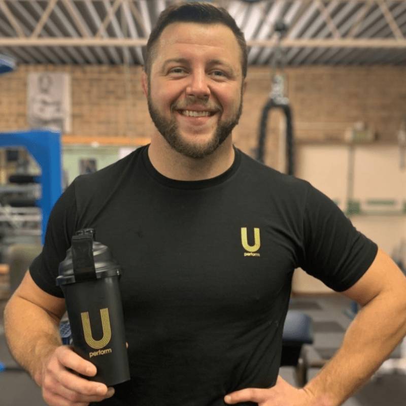 young man holding black and gold U Perform Shaker Bottle wearing black and gold U Perform Active T Shirt