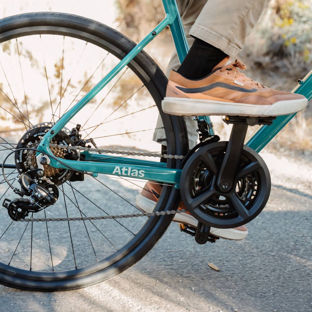 Close-up of a teal bicycle's rear wheel and drivetrain with a focus on the chain and gears, labeled "Atlas."