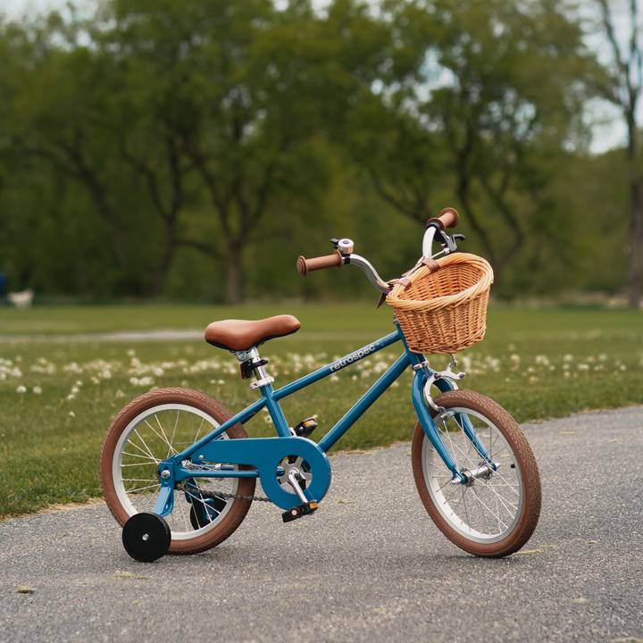 A blue Beaumont Mini 16" Kids' Bike with a wicker basket, brown handlebars, and training wheels parked on a pathway, surrounded by greenery.