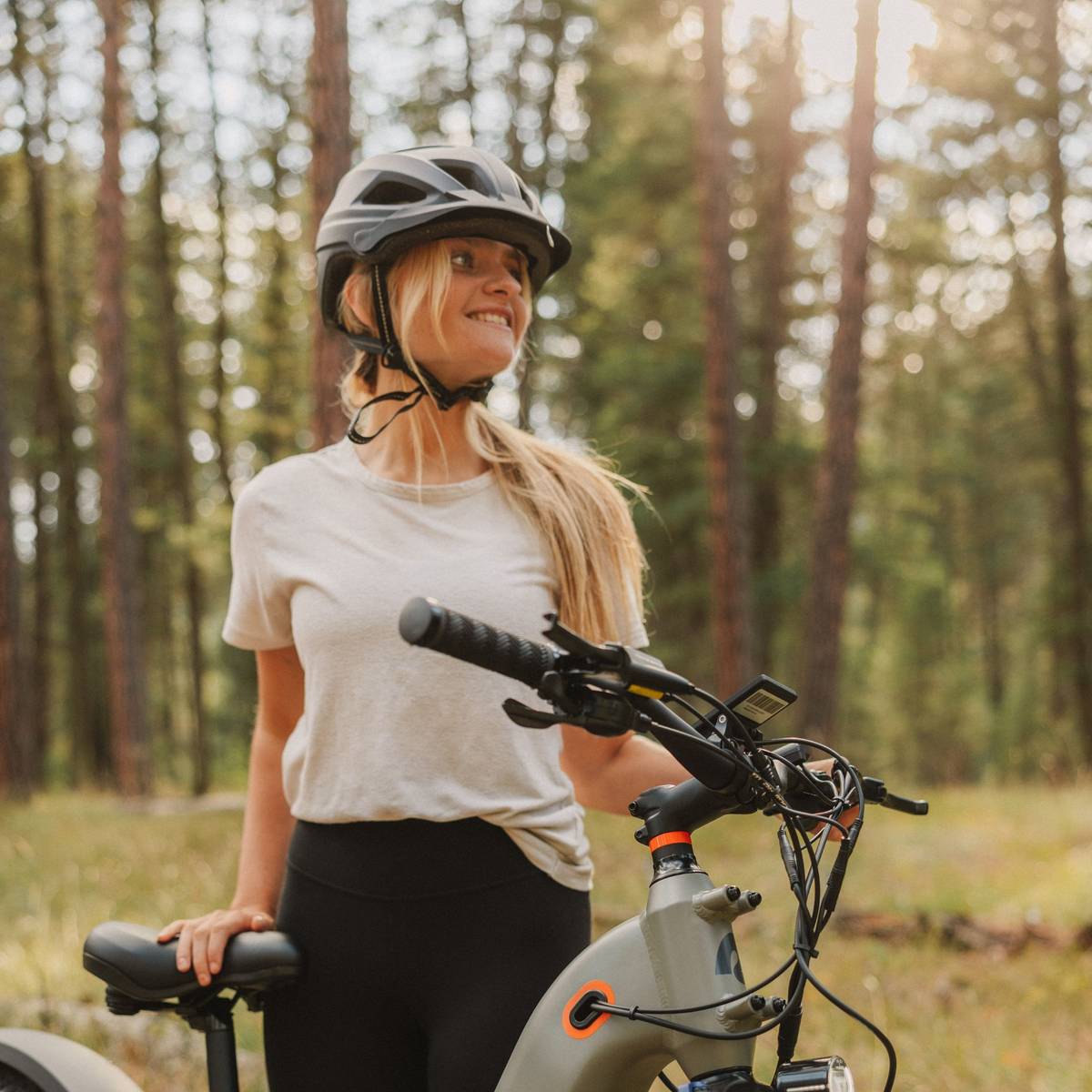 A woman wearing a Lennon Commuter Bike Helmet stands beside her electric bike, ready for a ride.