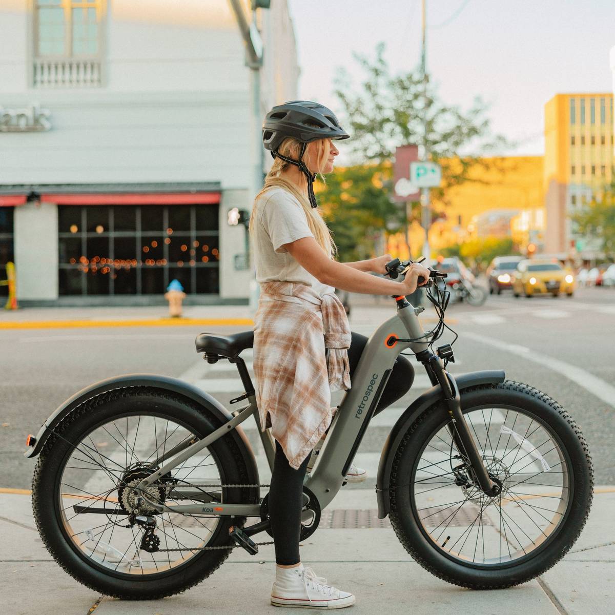 A woman on an electric bike navigates the street while wearing a Lennon Commuter Bike Helmet.