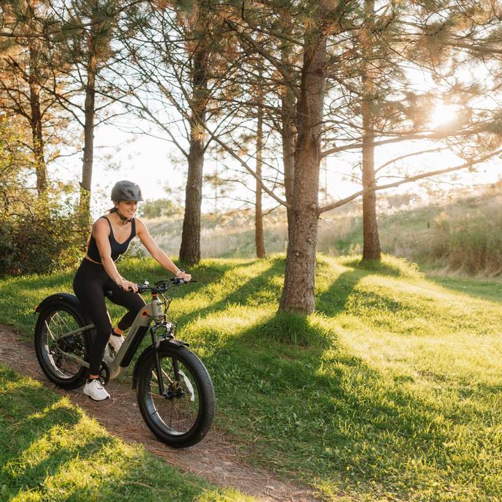 A woman rides a fat bike along a scenic trail surrounded by trees.