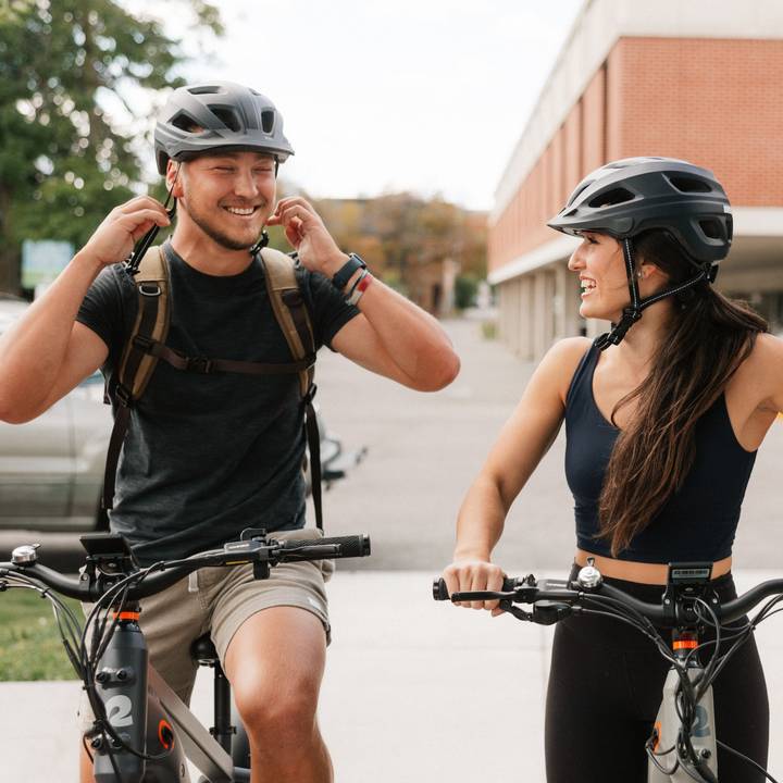 A man and woman on bicycles wearing Lennon Commuter Bike Helmets and talking while enjoying a sunny day outdoors.