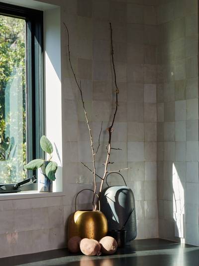 a kitchen wall corner covered in clé tile weathered white 4x4 tile with lots of shadows and brass flower vases