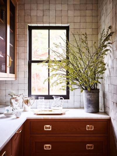 above a counter with a large floral arrangement is a kitchen wall covered in clé tile weathered white zellige 4x4 tile. 