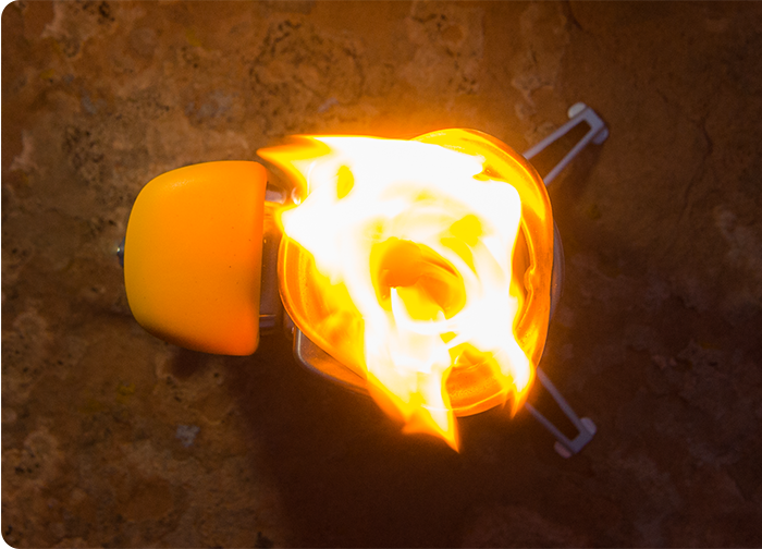 A top view of a yellow camping stove with flames erupting from the burner, set against a textured surface.