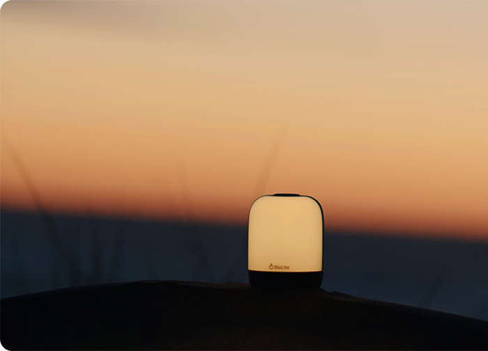 A soft-glowing lantern sits on a surface against a serene sunset backdrop, blending warm colors in the sky.