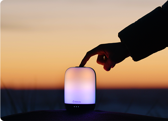 A hand touches a glowing lamp against a sunset backdrop, creating a serene atmosphere.