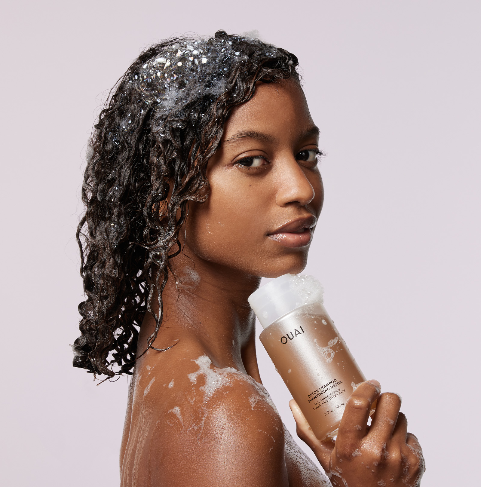 Woman with wet hair holding an OUAI product against a light background