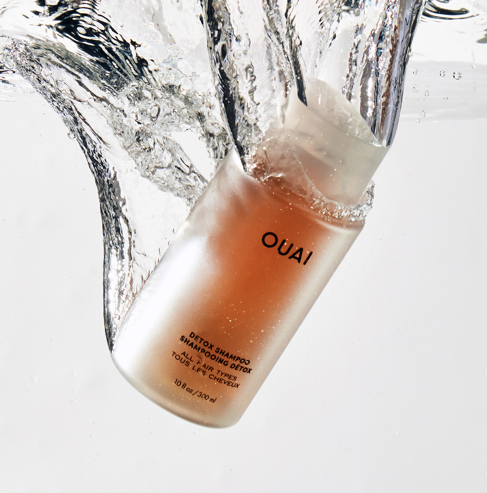 OUAI shampoo bottle with water splash on a light background
