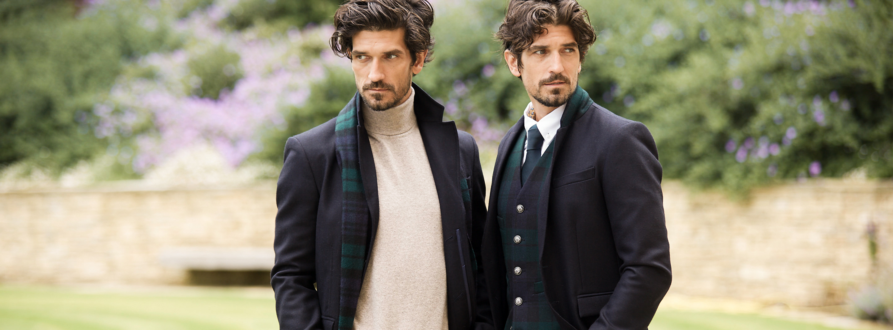 Two dark haired men stood side by side wearing navy coat and blazer with blackwatch scarf and waist coat