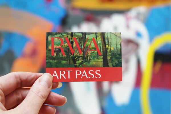 A hand holds a card that reads RWA Art Pass with a bright and bold abstract pattern in the background 