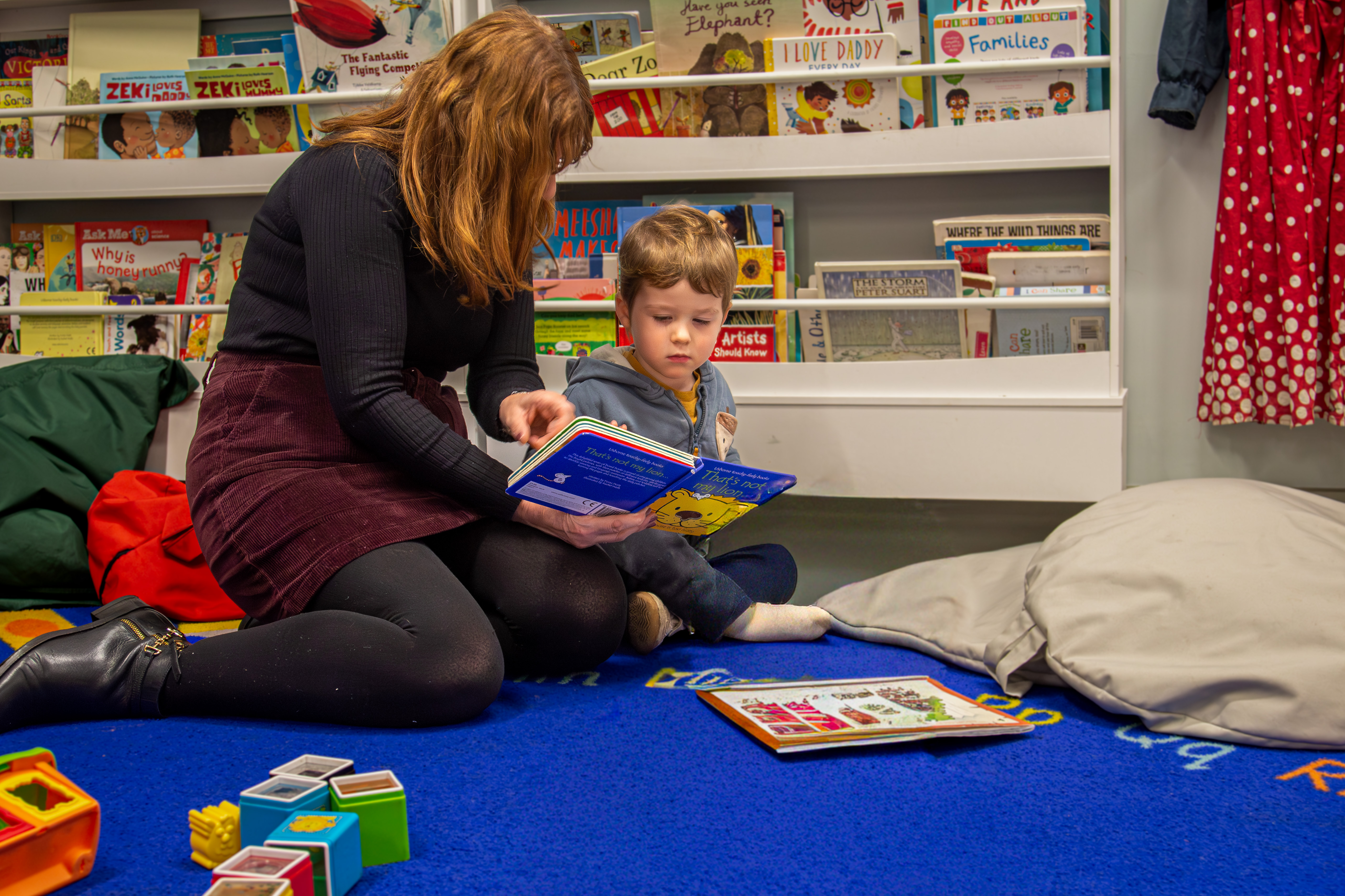 A woman reading to a little boy on the floor of our reading corner in the family room 