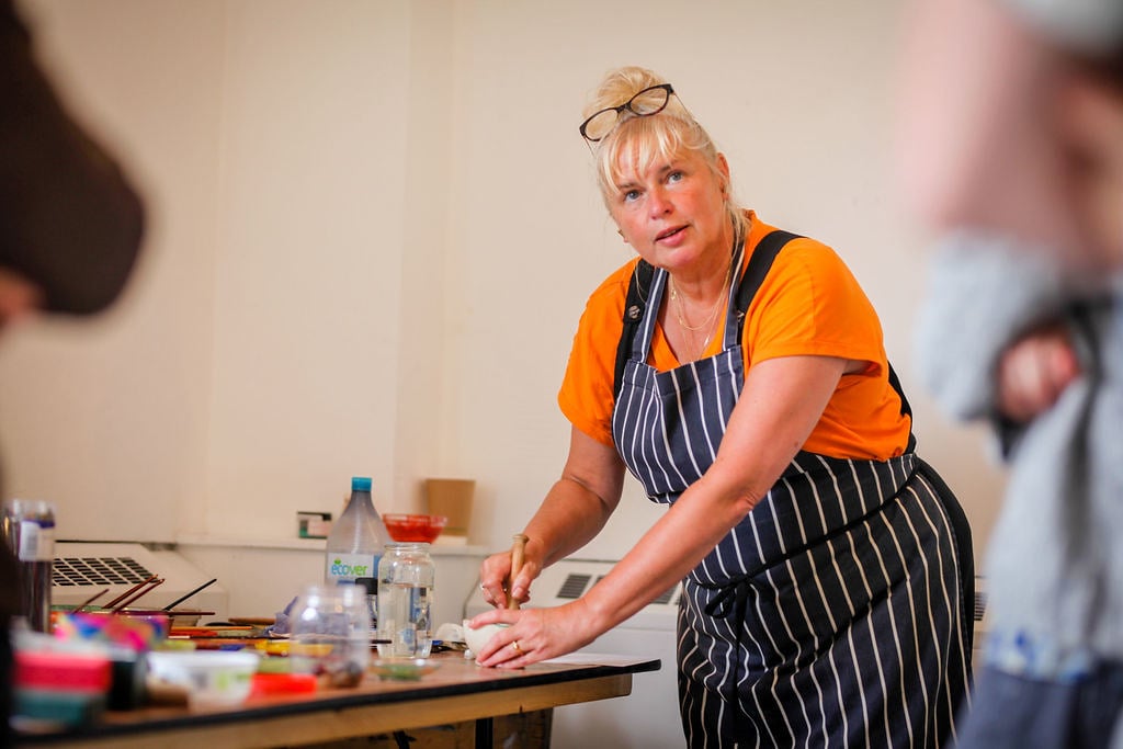 A woman with an apron on showing students how to mix pigments 