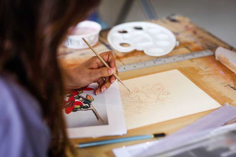 An image of a woman painting a flower 