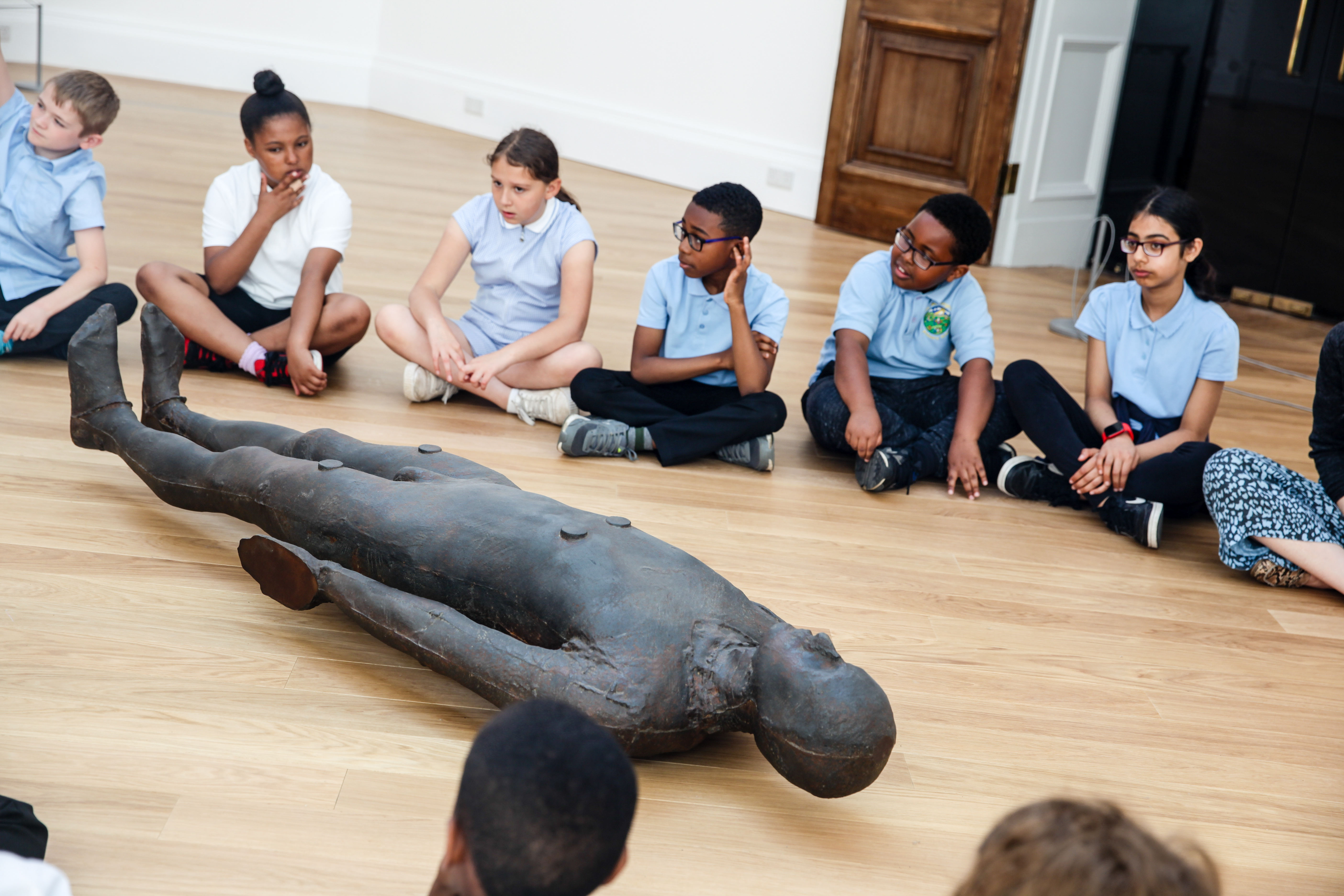 School children sat in a circle around a sculpture 