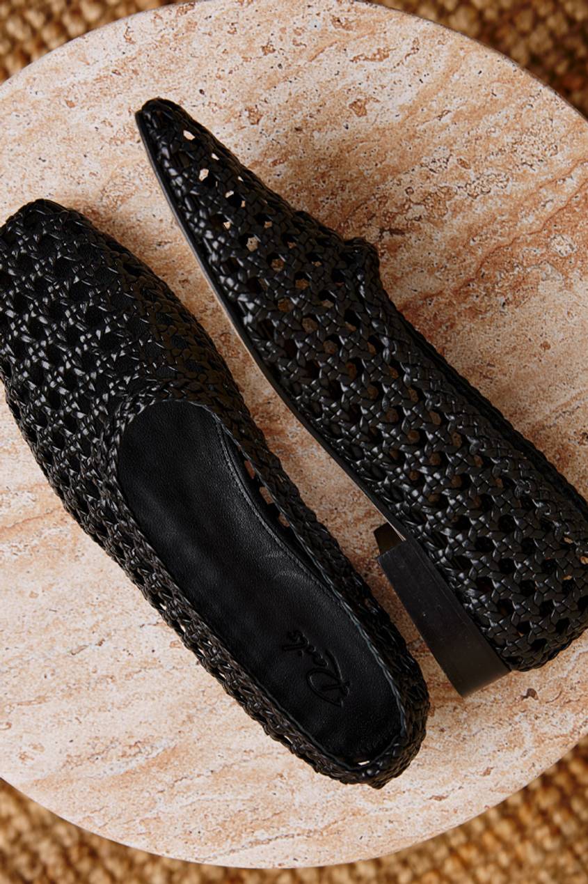 Close up image of black woven ballet flats displayed on a marble textured surface.