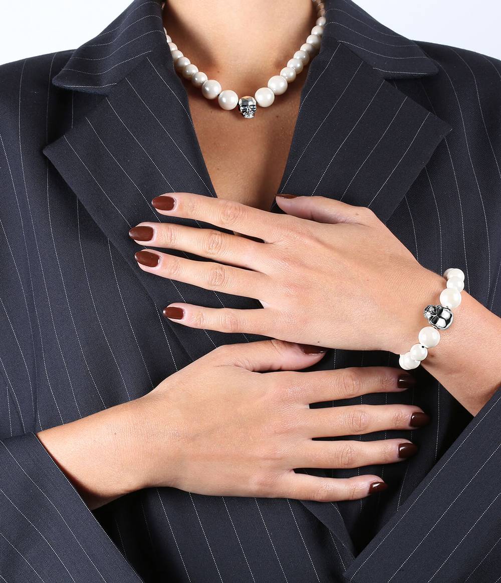 A girl with a stripped blazer is wearing a silver skull and pearl necklace and a matching bracelet.